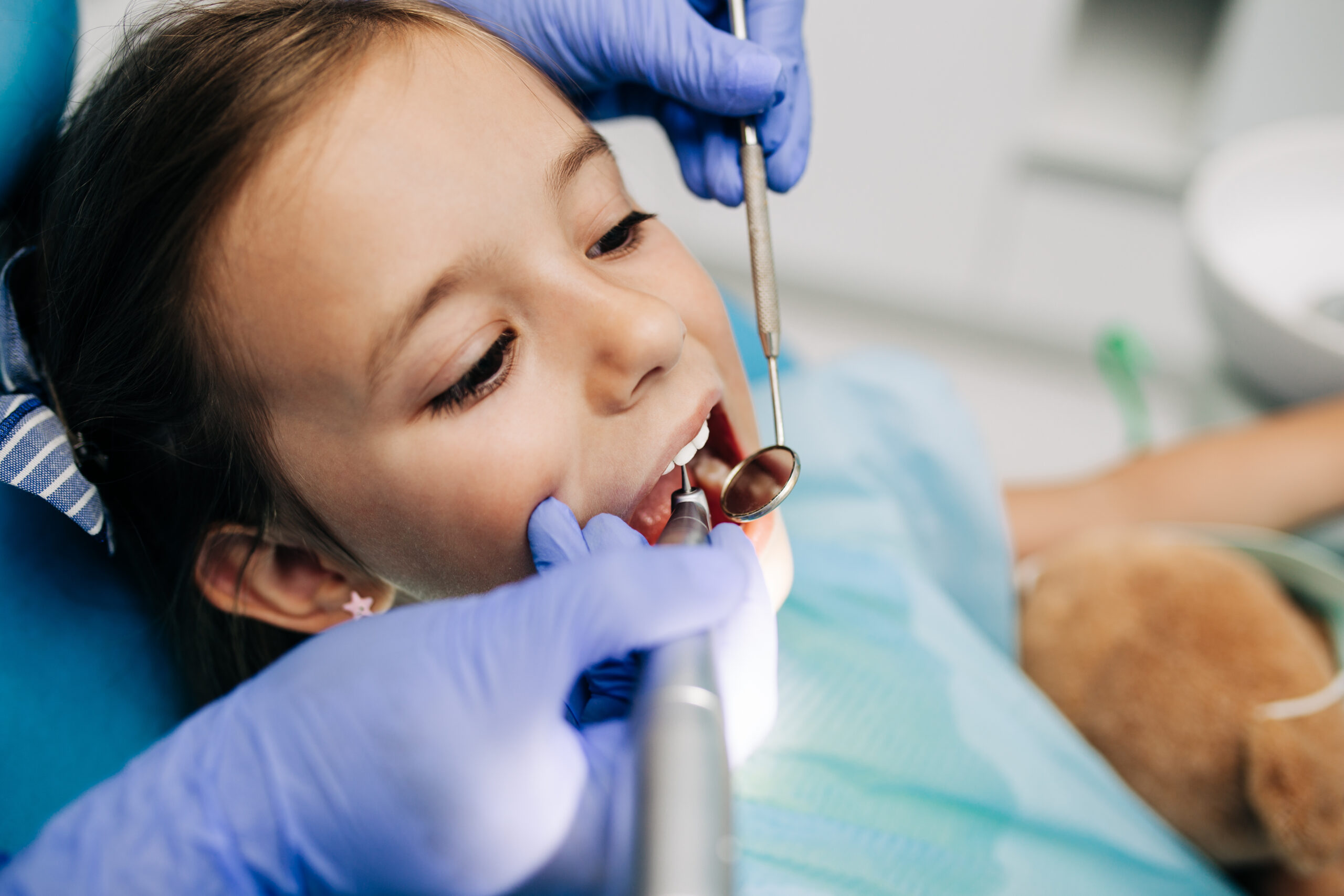 Cute little girl sitting on dental chair and having dental treatment.