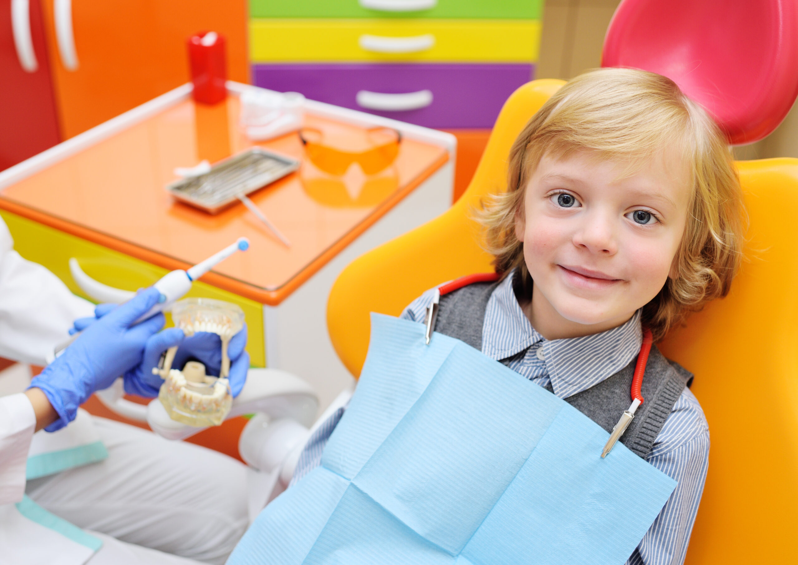 smiling baby boy with blond curly hair in dental chair. Pediatric dentistry.
