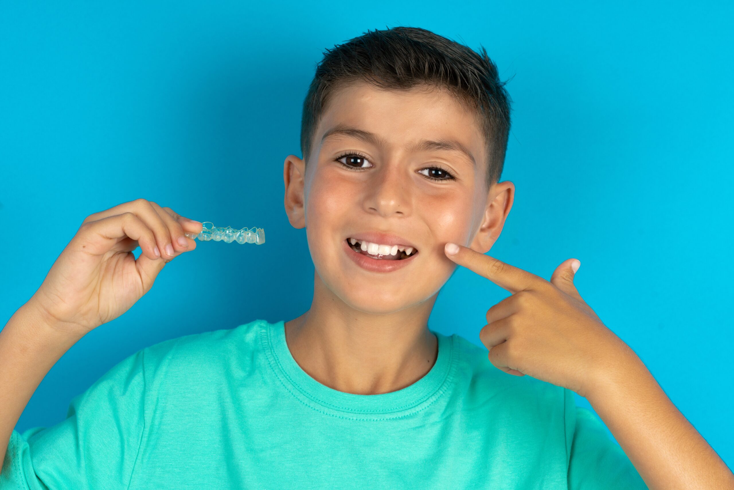 MODEL holding an invisible aligner and pointing to her perfect straight teeth. Dental healthcare and confidence concept.