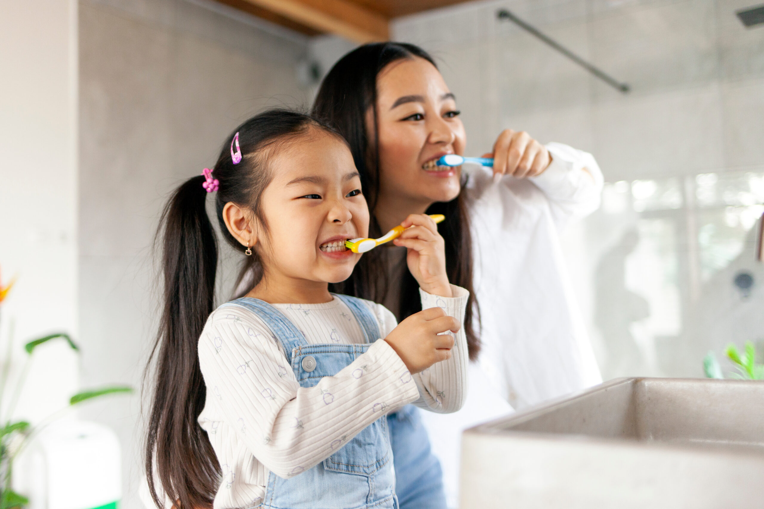 asian little girl with mom brushing teeth in bathroom, korean woman helping to brush daughter's teeth at home together, asian family and hygiene procedures