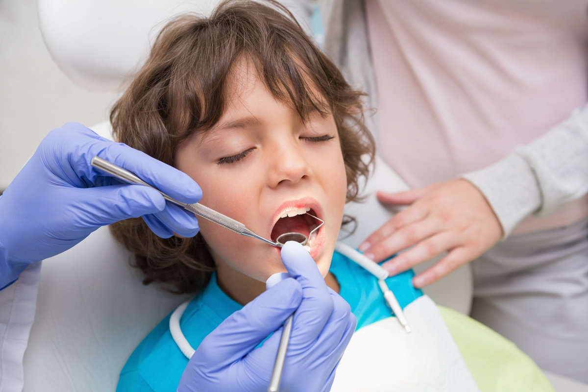 Pediatric dentist examining a little boys teeth with his mother