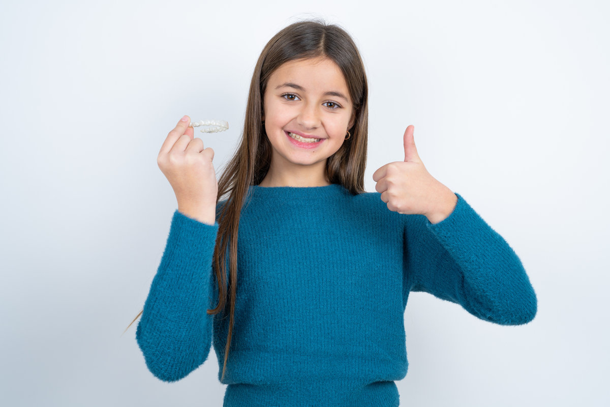 MODEL holding an invisible braces aligner and rising thumb up, recommending this new treatment. Dental healthcare concept.
