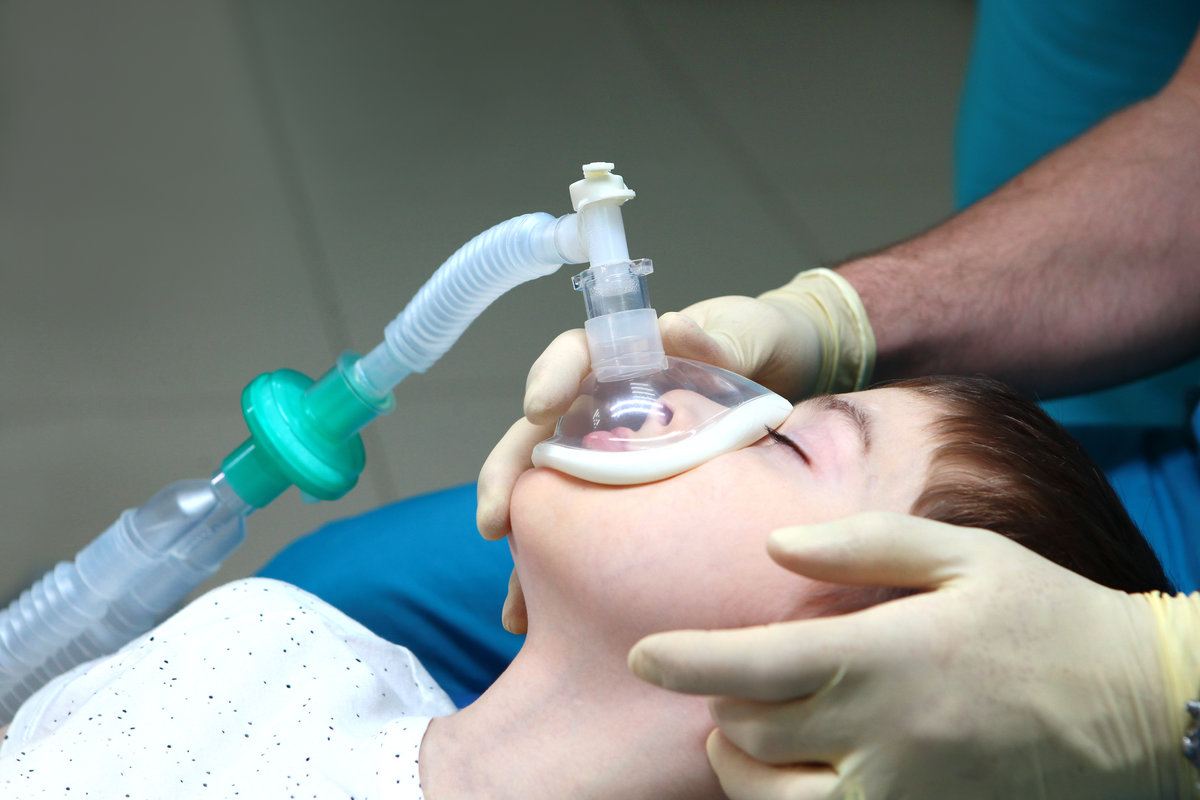 Child with an oxygen mask on his face. Preparing child for anesthesia. Dental treatment under general anesthesia. Dental surgery under general anesthesia. Surgical intervention. Side view.