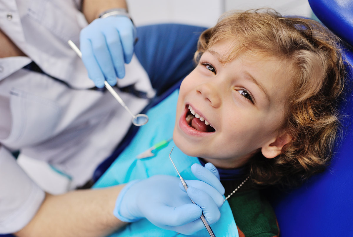 smiling child sitting in a blue chair dental