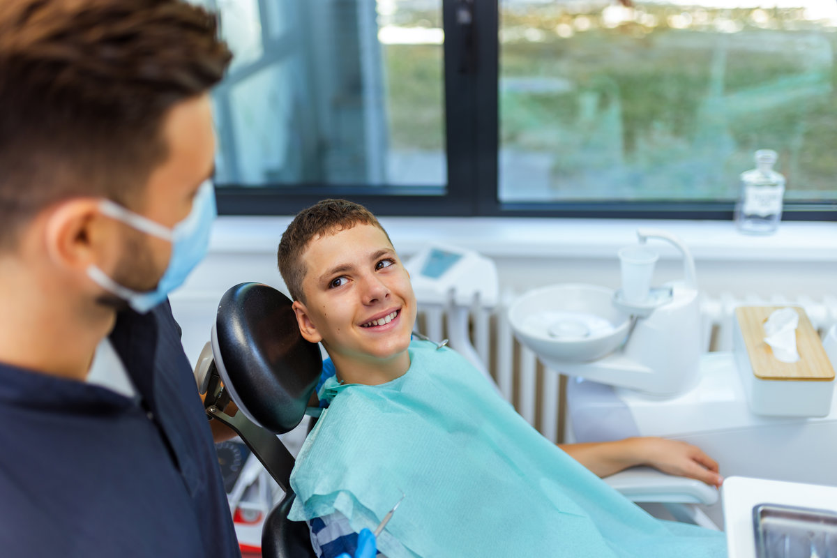 Little boy sits in a dental chair at a modern clinic while the dentist prepares to examine and repair his teeth, showing pediatric care and professional treatment.