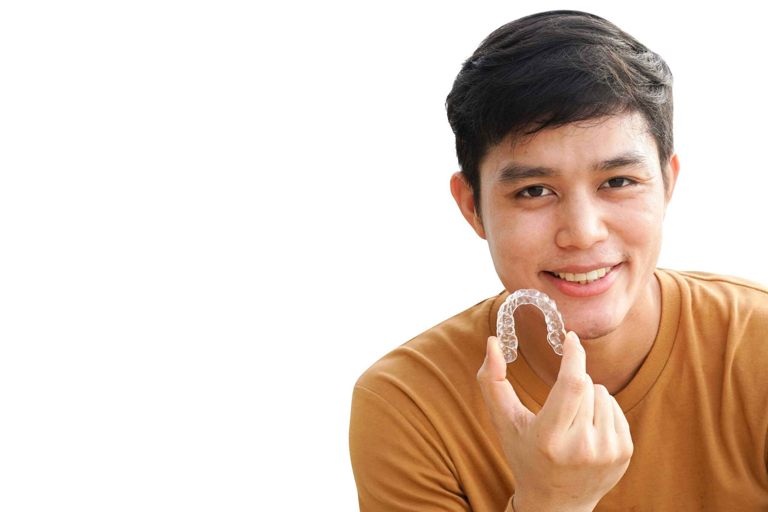 Young man smiling and holding a clear dental aligner at a dental clinic