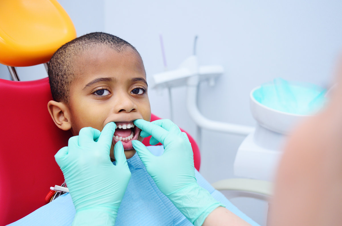 cute black baby boy African American smiling sitting in the dental chair at the examination at the children's dentist.