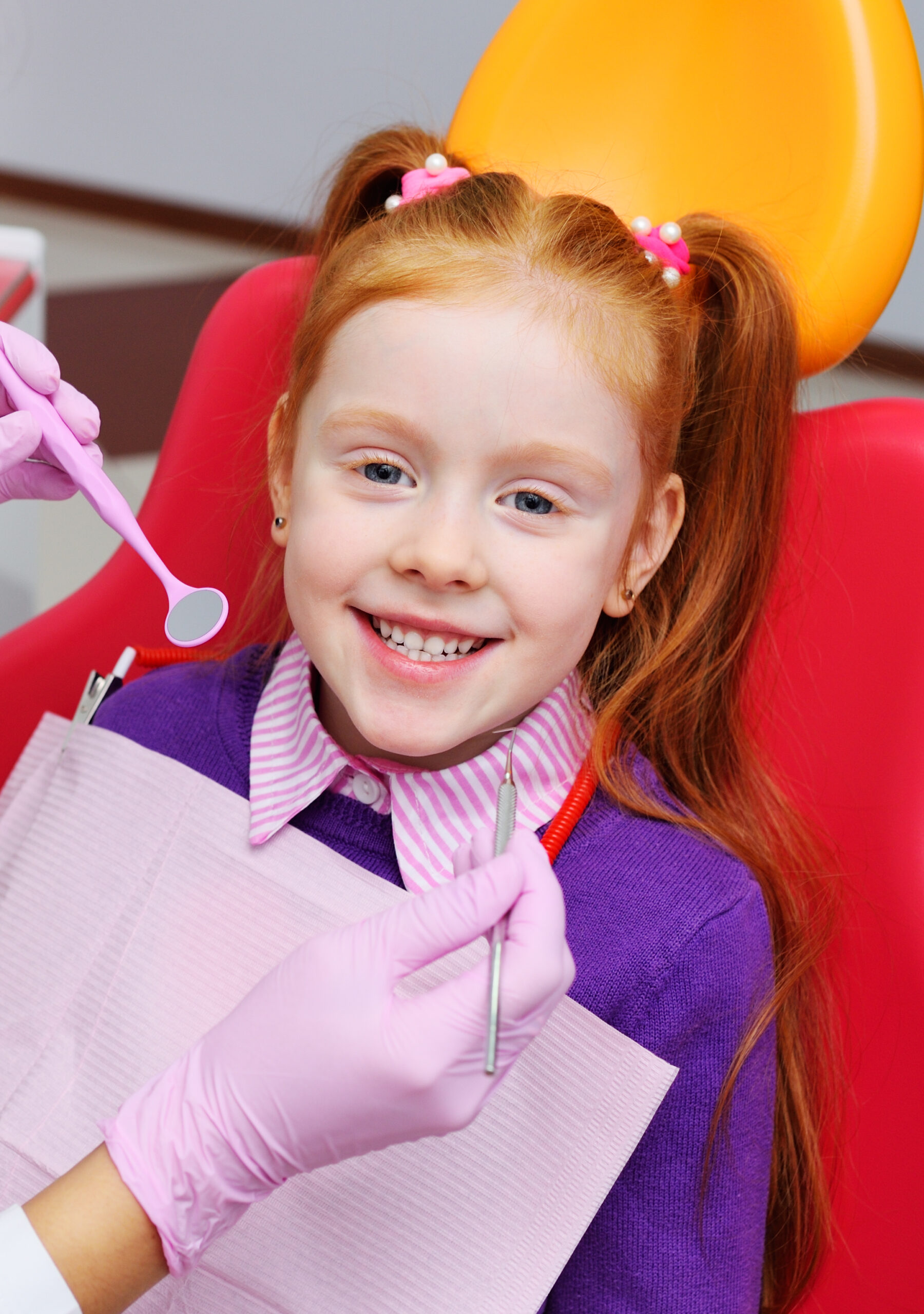 children's dentist examines the teeth and mouth of the child - a cute red-haired girl sitting in a dental chair. Pediatric dentistry