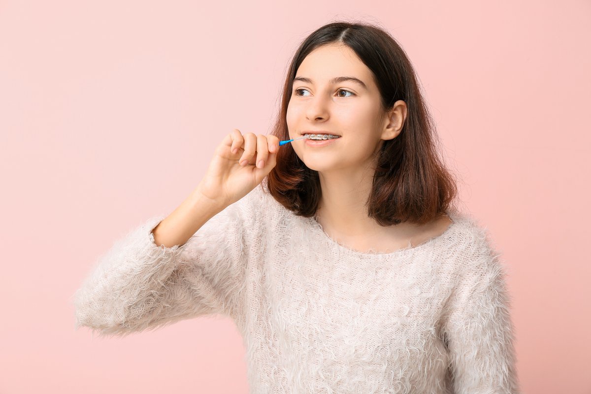 Teenage girl with dental braces and toothbrush smiling at pediatric dentist near Boerne